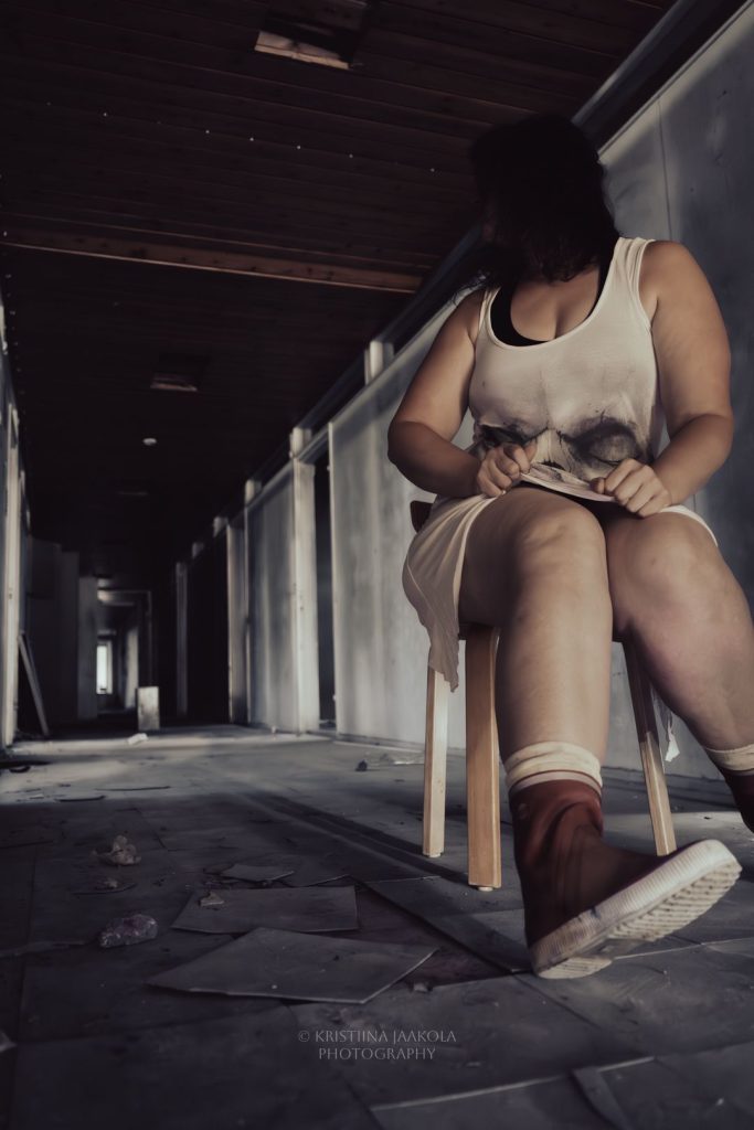 Annen kuva tuo mieleen kauhuelokuvan kohtauksen. Anne istuu tuolilla karussa, ränstisyneessä rakennuksessa vilkuillen taakseen.